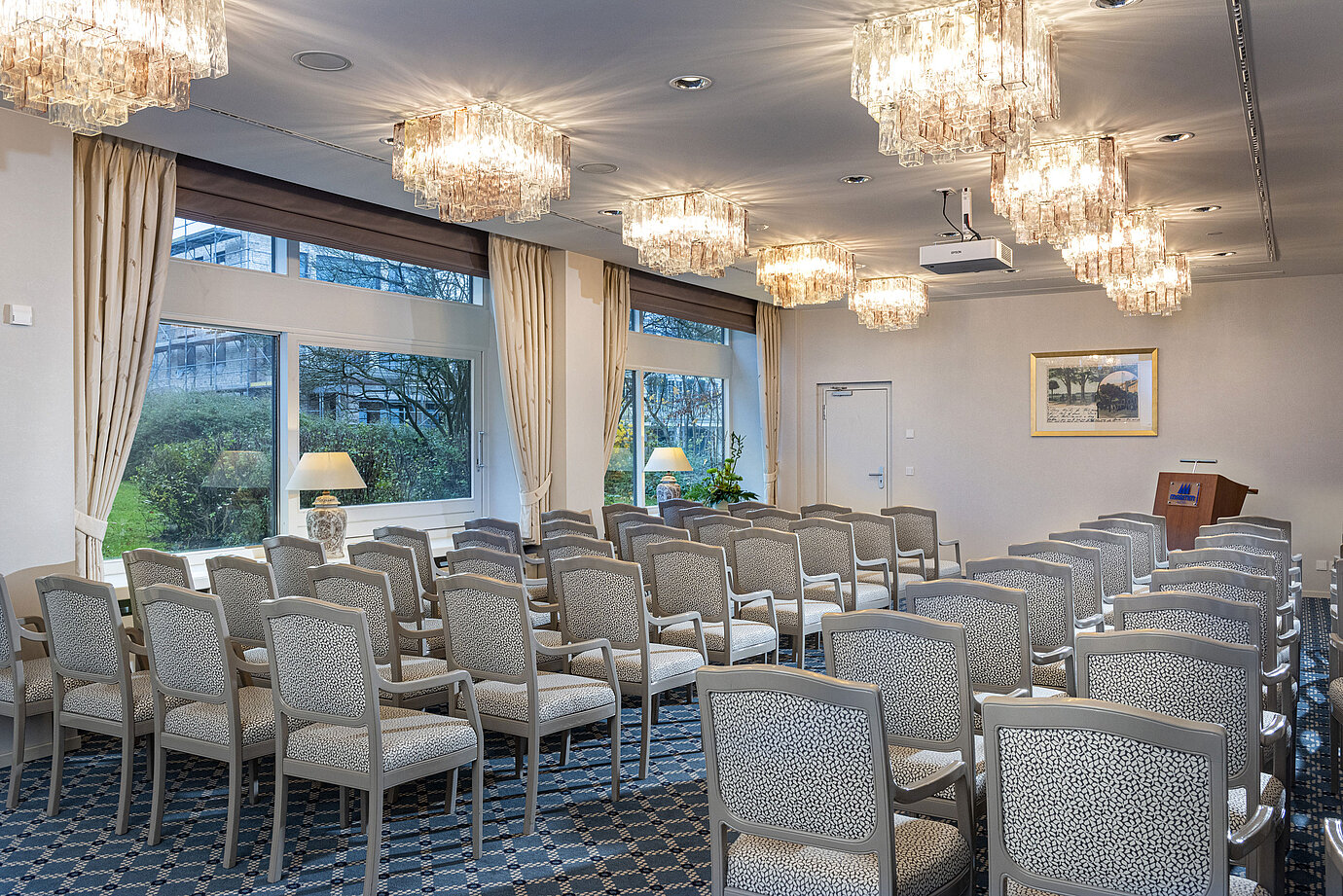 Salon Helsinki in the Maritim Hotel Kiel, conference room with rows of chairs, chandeliers and large windows with a view of the greenery.