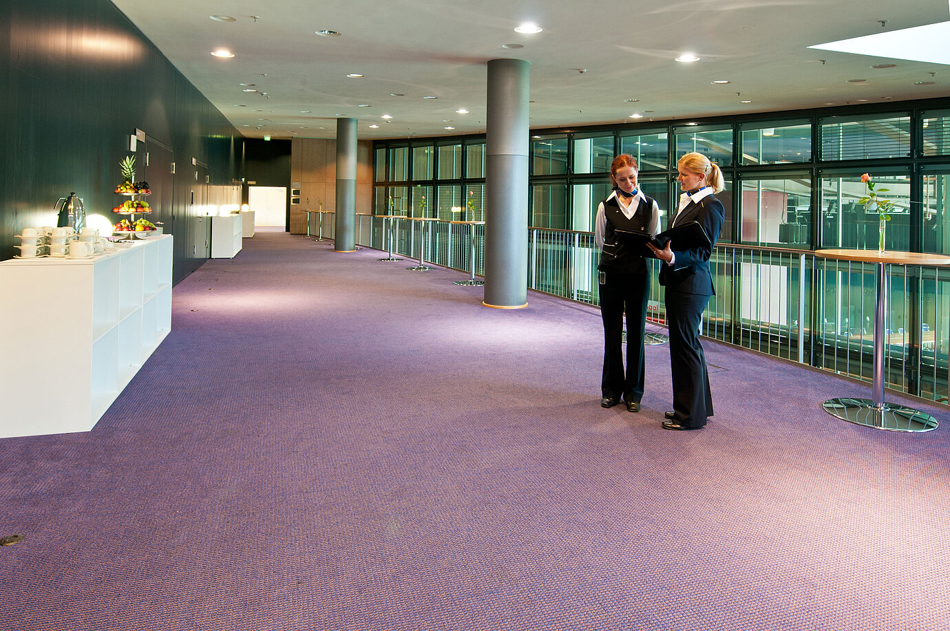 Foyer in Maritim Hotel Dresden with two staff members in uniform, standing tables, and a fruit station.