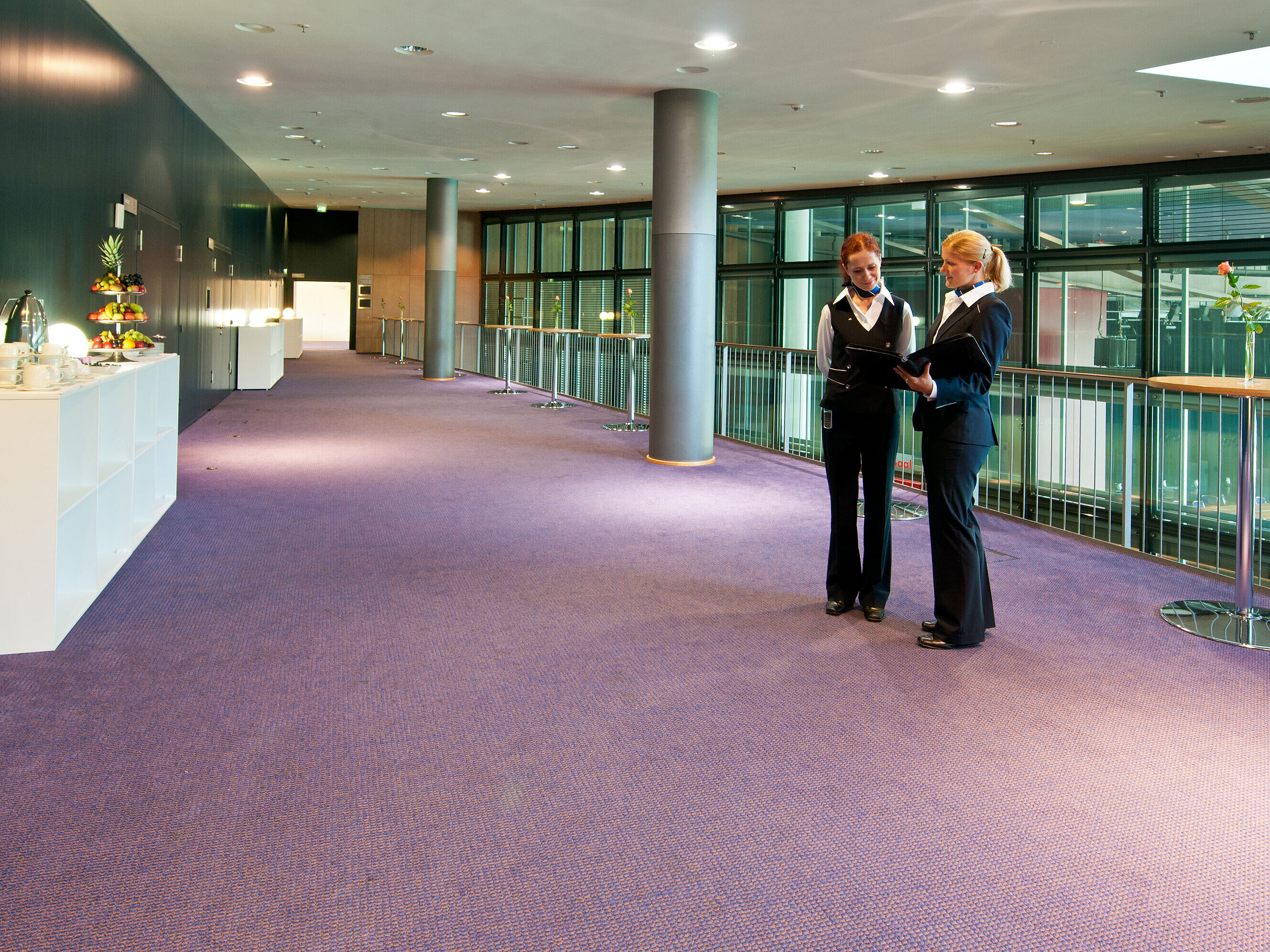 Foyer in Maritim Hotel Dresden with two staff members in uniform, standing tables, and a fruit station.