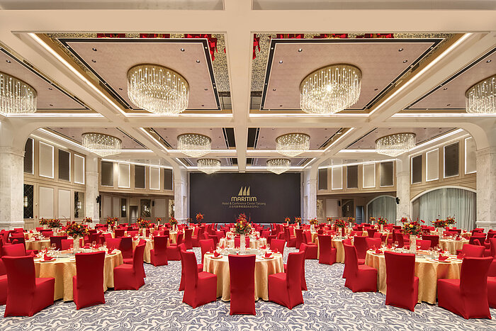 Festive banquet hall at Maritim Hotel with red chairs, gold tables and elegant chandeliers