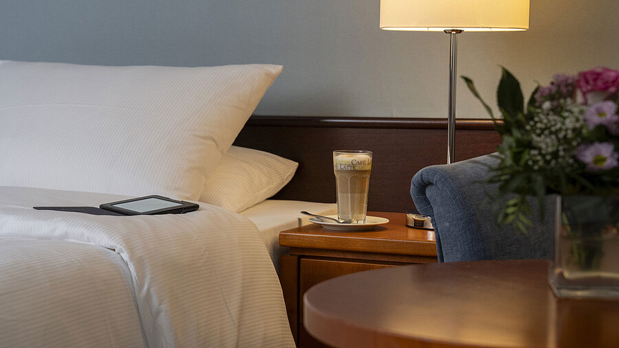 Close-up of a cozy Classic room at Maritim Hotel Darmstadt with a bed, bedside table, latte macchiato, and modern lighting.