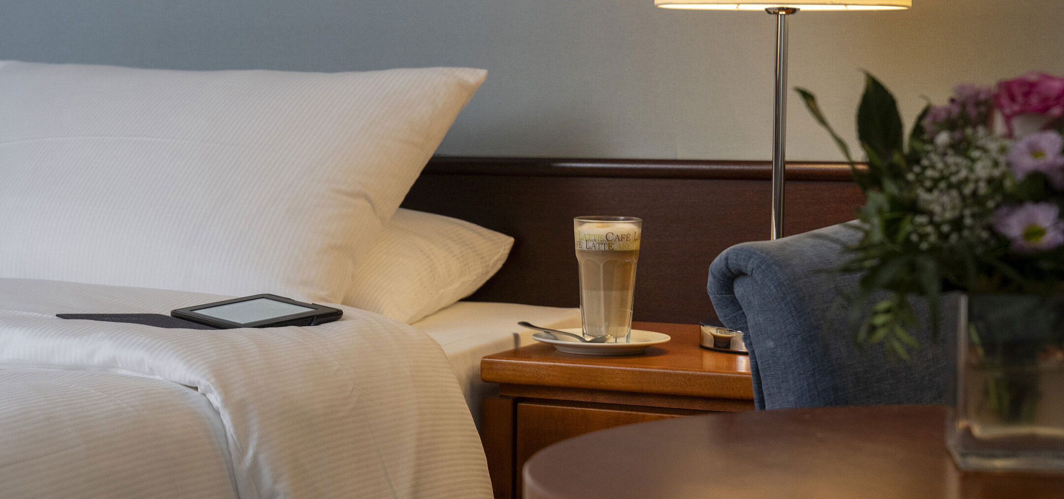 Close-up of a cozy Classic room at Maritim Hotel Darmstadt with a bed, bedside table, latte macchiato, and modern lighting.