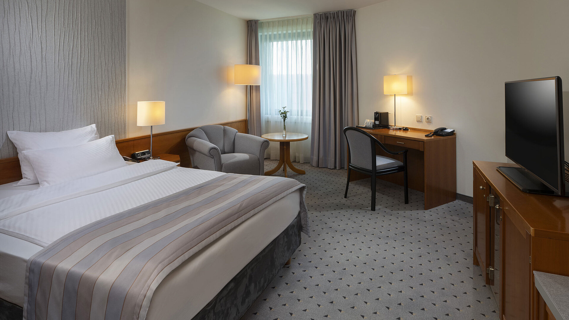 Spacious superior room with bed, desk, TV, and warm lighting design at Maritim Hotel Hannover.