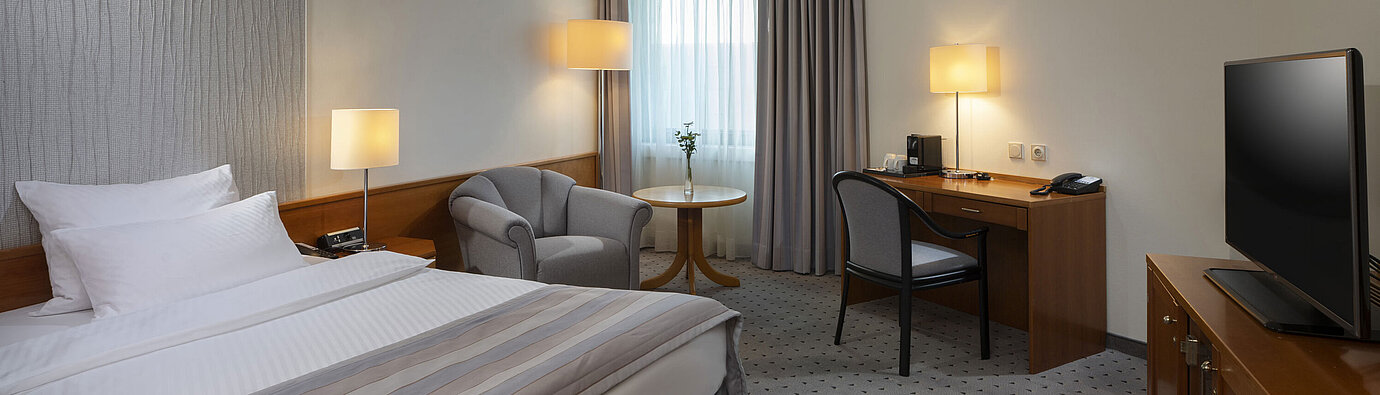 Spacious superior room with bed, desk, TV, and warm lighting design at Maritim Hotel Hannover.