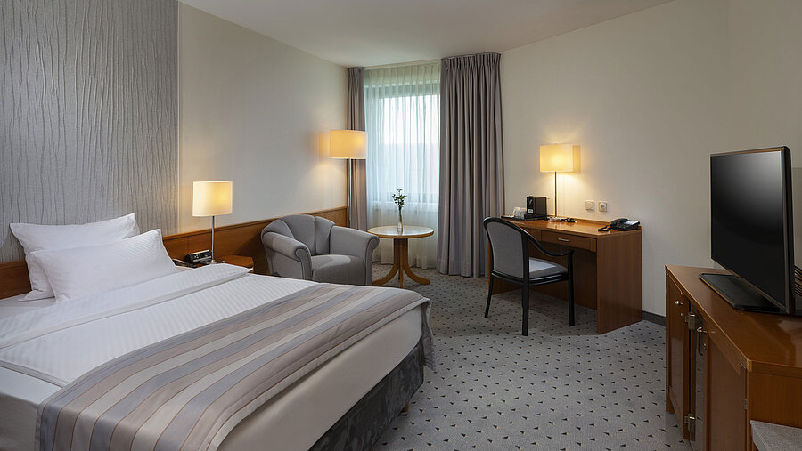 Spacious superior room with bed, desk, TV, and warm lighting design at Maritim Hotel Hannover.
