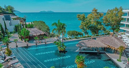 Large pool area at Maritim Resort Marina Bay with palm trees, sea view and stylish relaxation zones