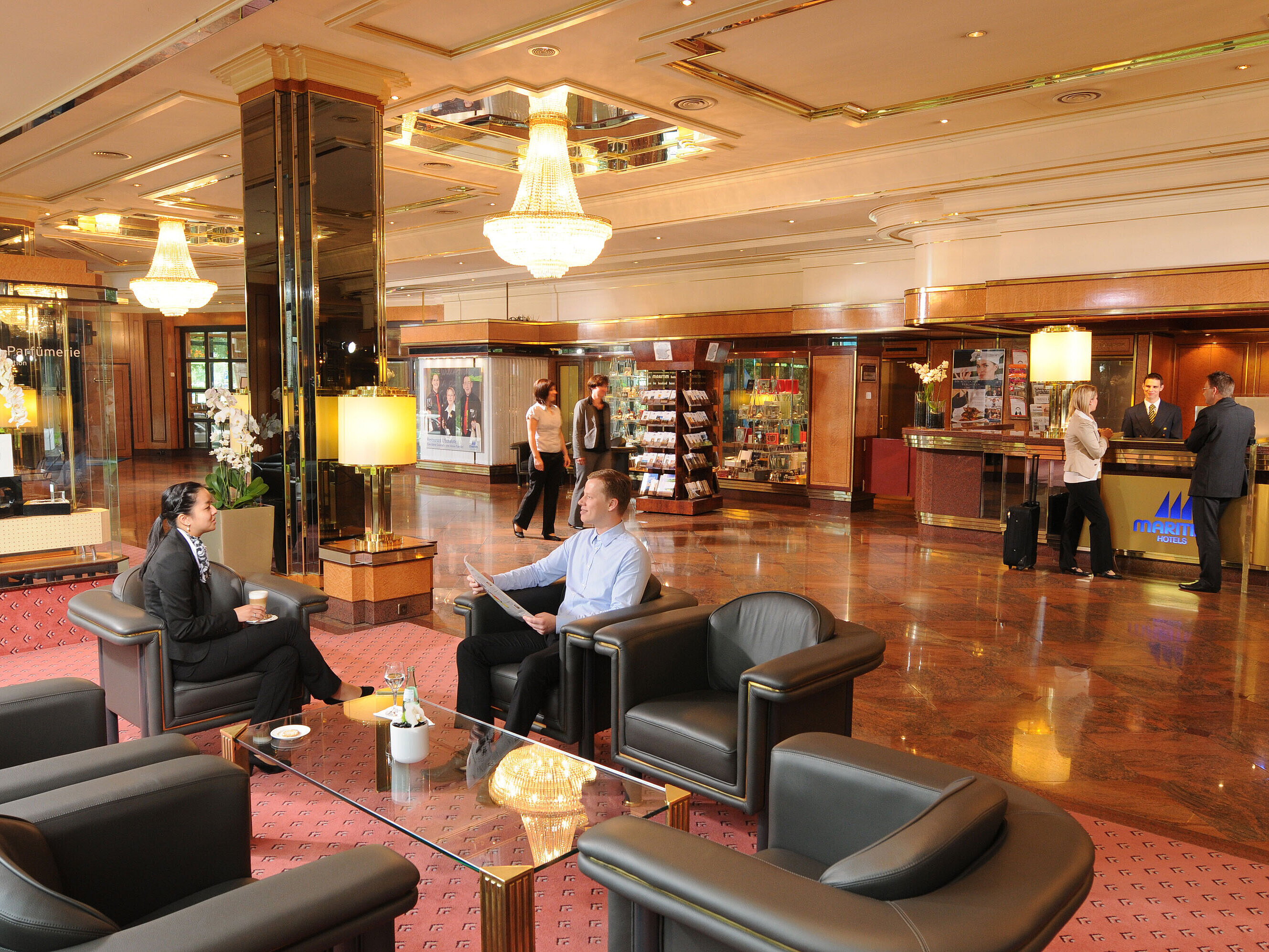 Spacious lobby at Maritim Hotel Bremen with elegant seating, guests conversing, and reception staff at the check-in desk.