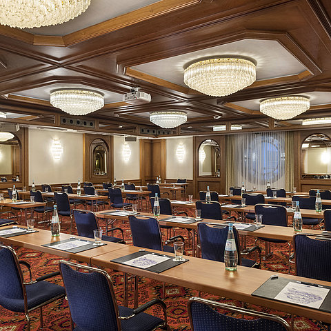 The Cologne Hall with elegant chandeliers and seating rows in a classic conference room setting, ready for a meeting.