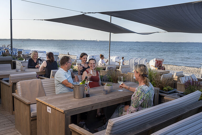 Group of guests at the beach bar of Maritim Seehotel Timmendorfer Strand enjoying drinks with sea view and beach chairs.