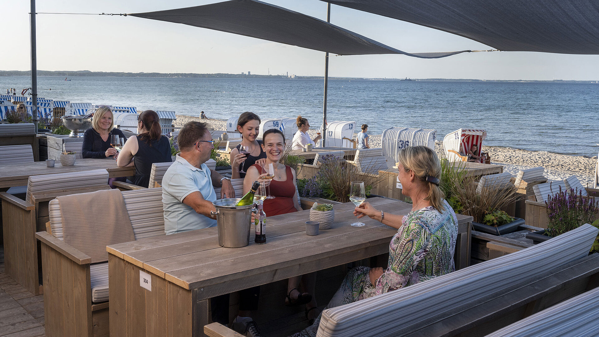 Group of guests at the beach bar of Maritim Seehotel Timmendorfer Strand enjoying drinks with sea view and beach chairs.