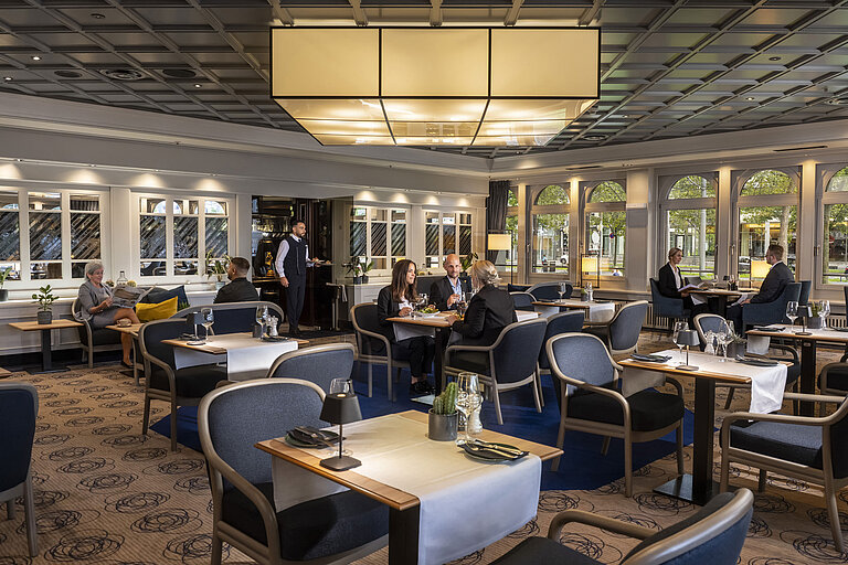 Elegant restaurant at Maritim Hotel Darmstadt with guests dining and relaxing. Modern decor and large windows with a view.