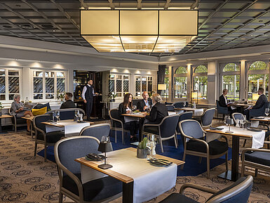 Elegant restaurant at Maritim Hotel Darmstadt with guests dining and relaxing. Modern decor and large windows with a view.