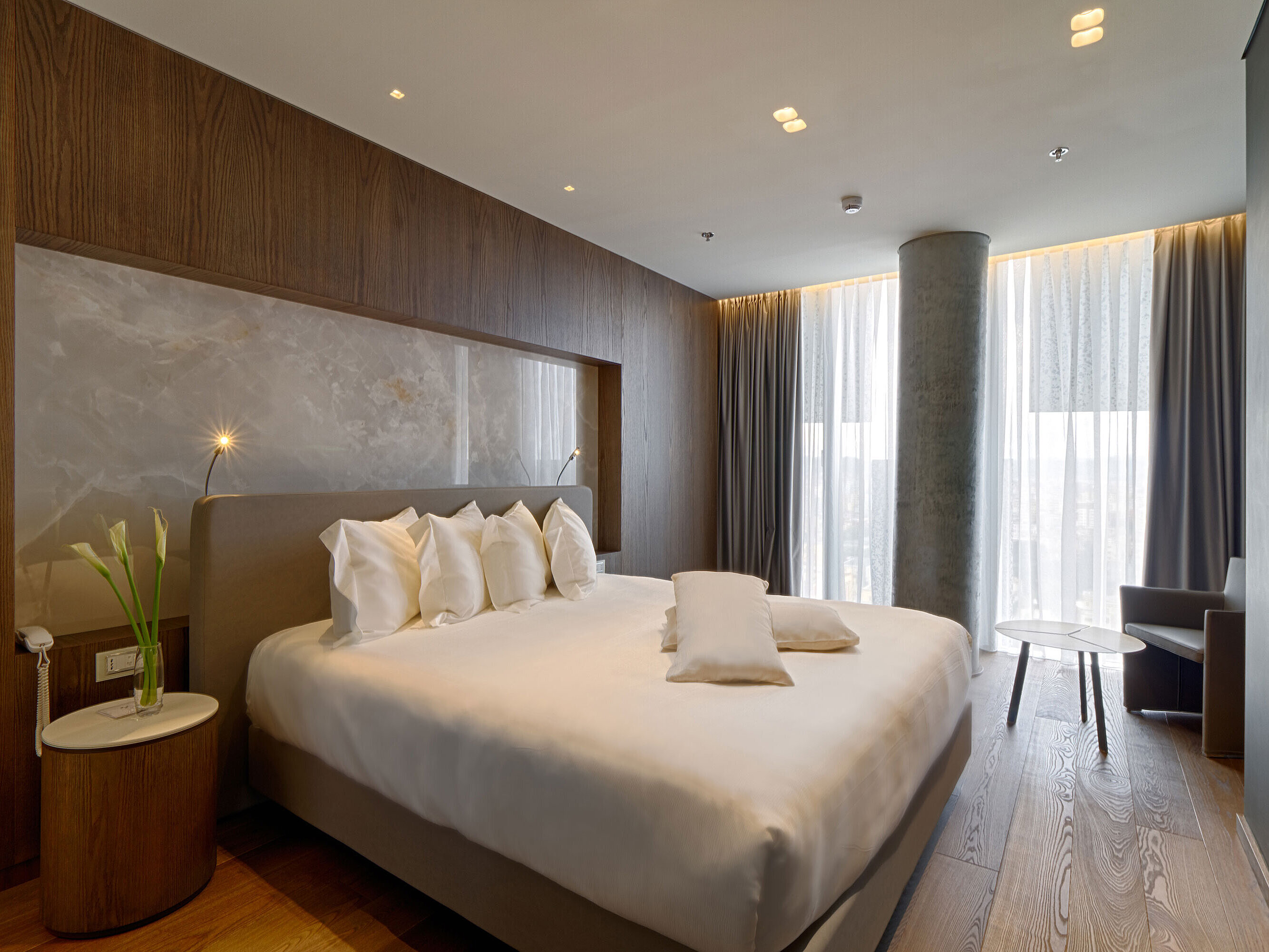 Quiet room with large bed, natural stone wall and soft curtains at Maritim Hotel Plaza Tirana