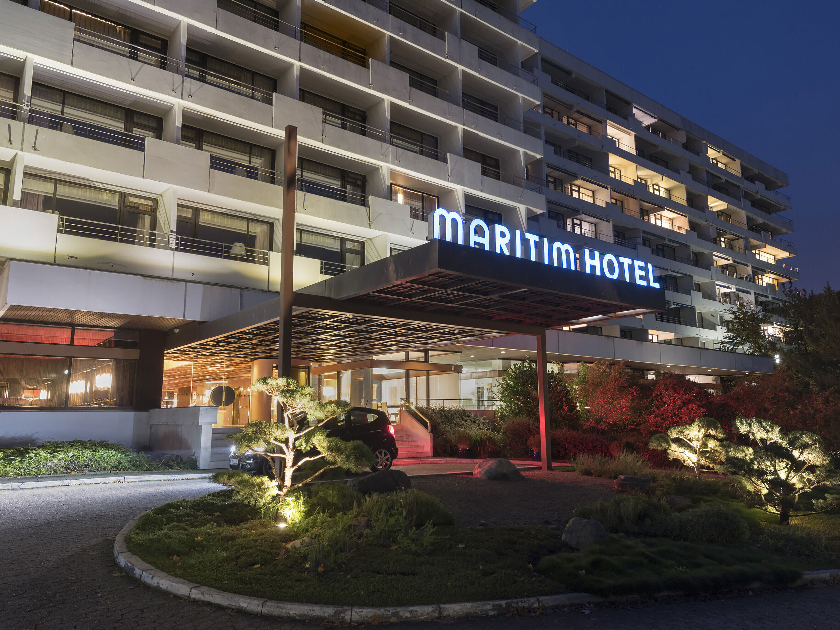 Exterior view of the Maritim Hotel Kiel at night, illuminated hotel entrance and modern architecture with balconies and well-kept garden.