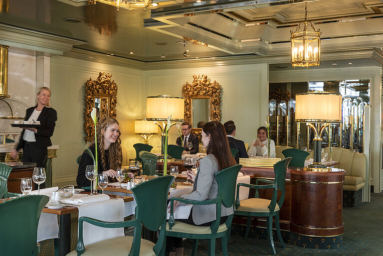 Guests enjoying their meal in the "La Galerie" restaurant at Maritim Hotel Cologne, surrounded by stylish mirrors and lamps.
