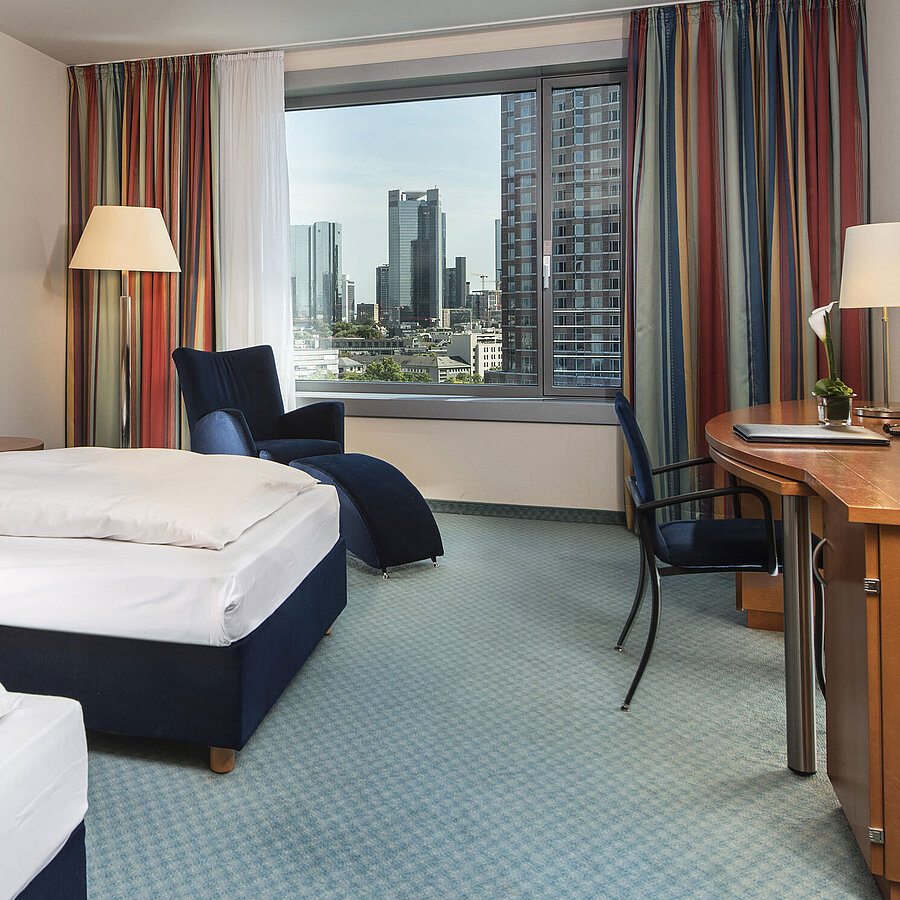 Comfort room at Maritim Hotel Frankfurt with two single beds, desk, seating area, and skyline view.