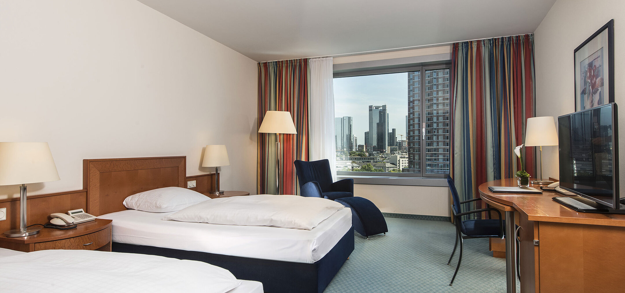 Comfort room at Maritim Hotel Frankfurt with two single beds, desk, seating area, and skyline view.