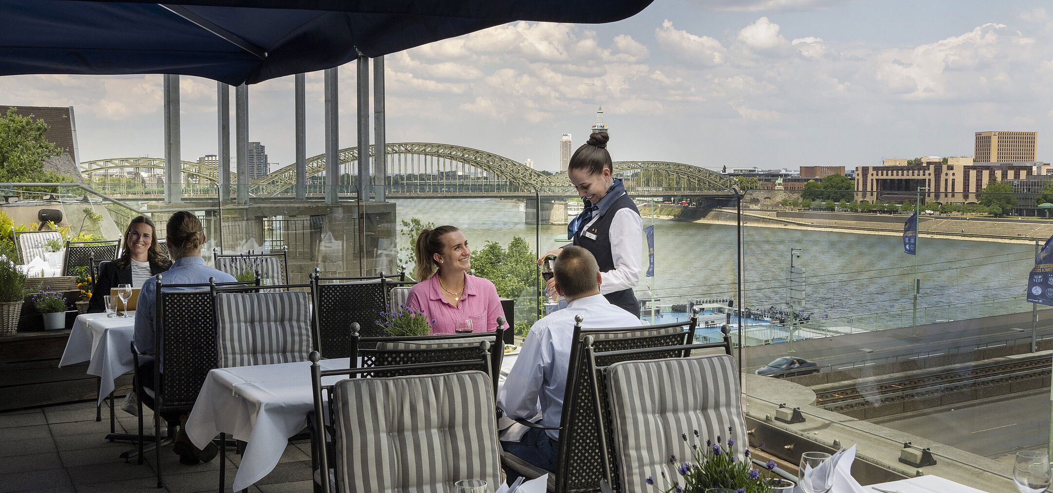 Guests enjoying service on the rooftop terrace of Maritim Hotel Cologne with views of the Rhine River and Hohenzollern Bridge
