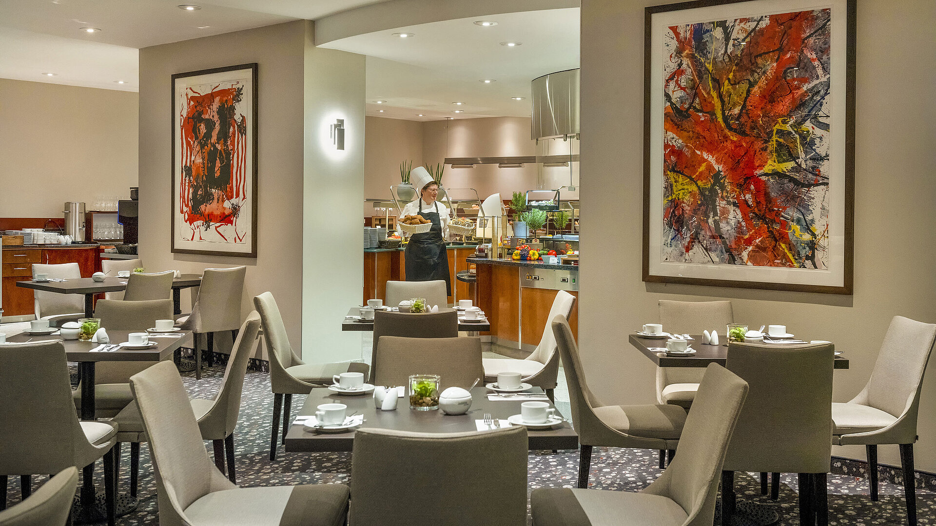 Restaurant at Maritim proArte Hotel Berlin with modern art on walls, set tables, and a chef at the buffet.