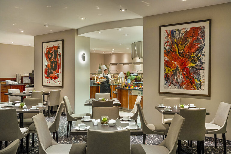 Restaurant at Maritim proArte Hotel Berlin with modern art on walls, set tables, and a chef at the buffet.