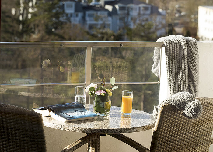 Balcony table with drinks, book, and flowers at Maritim Seehotel Timmendorfer Strand overlooking trees and buildings.