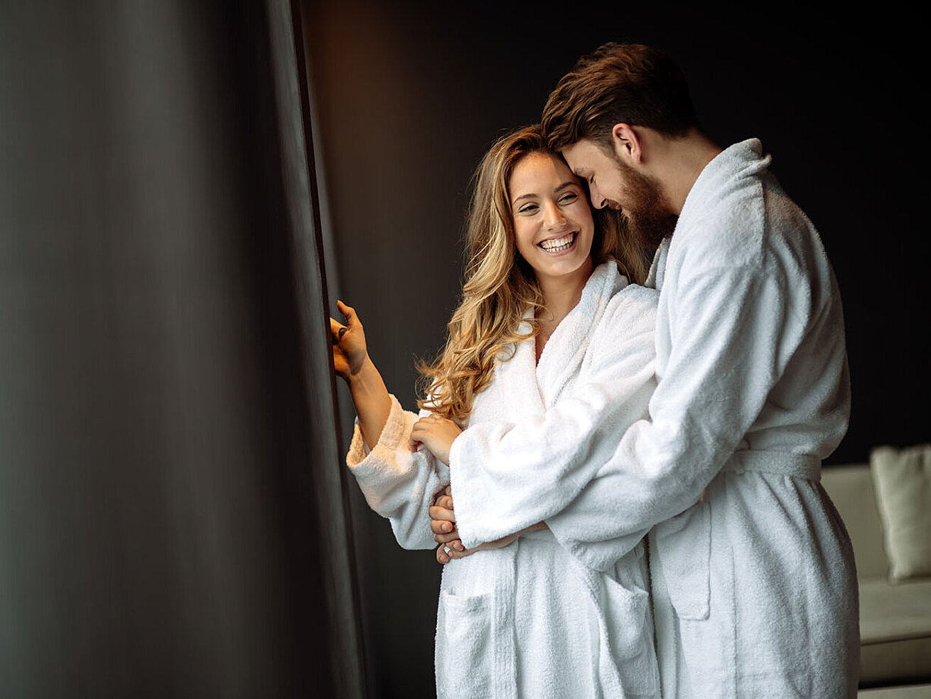 Couple in bathrobes standing by the window smiling and enjoying a relaxing hotel moment
