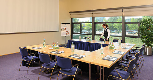 Meeting room in Maritim Hotel Dresden with U-shaped table setup, presentation screen, and meeting preparations.