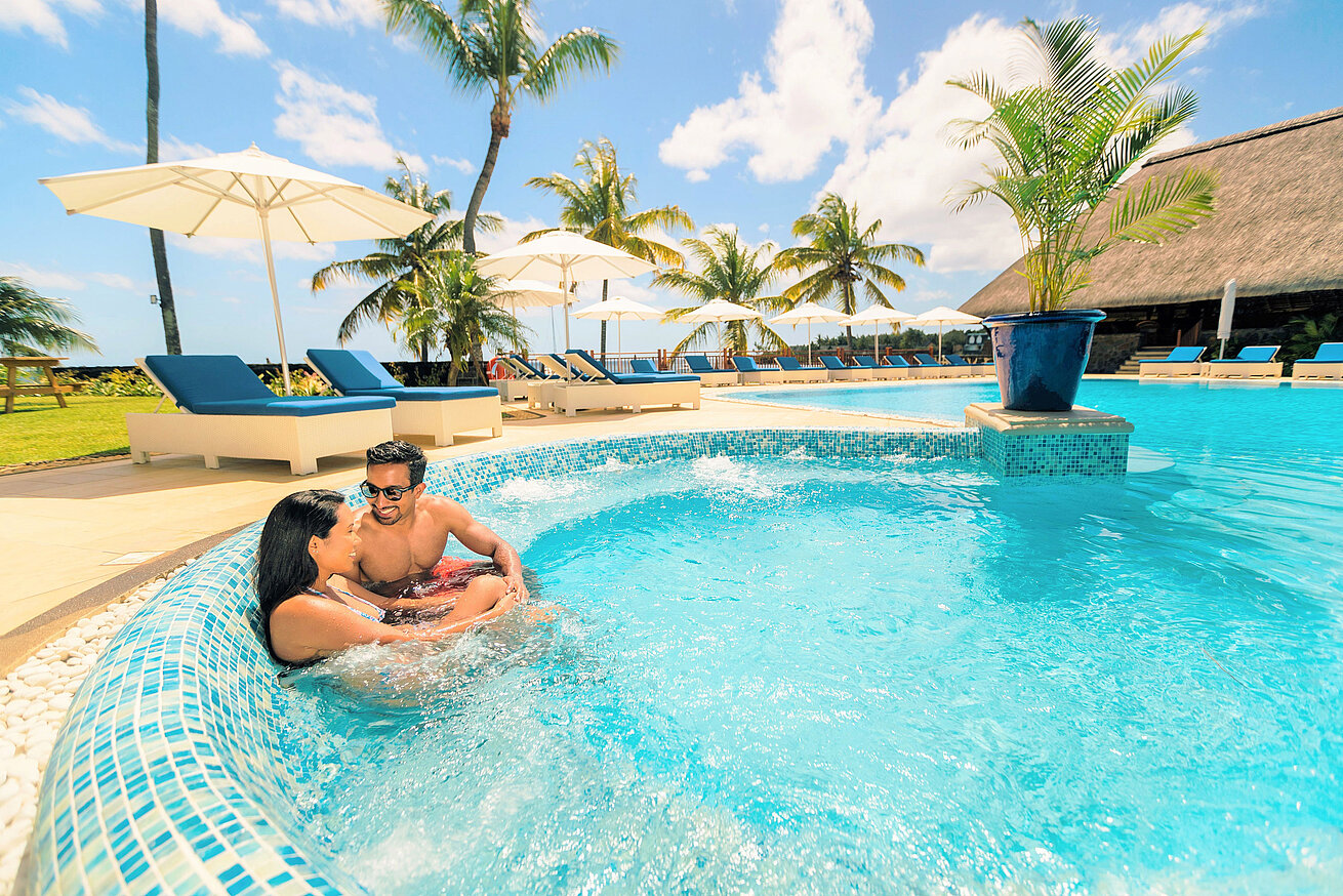 Couple relaxing in hotel pool with palm trees, sun umbrellas and blue sky