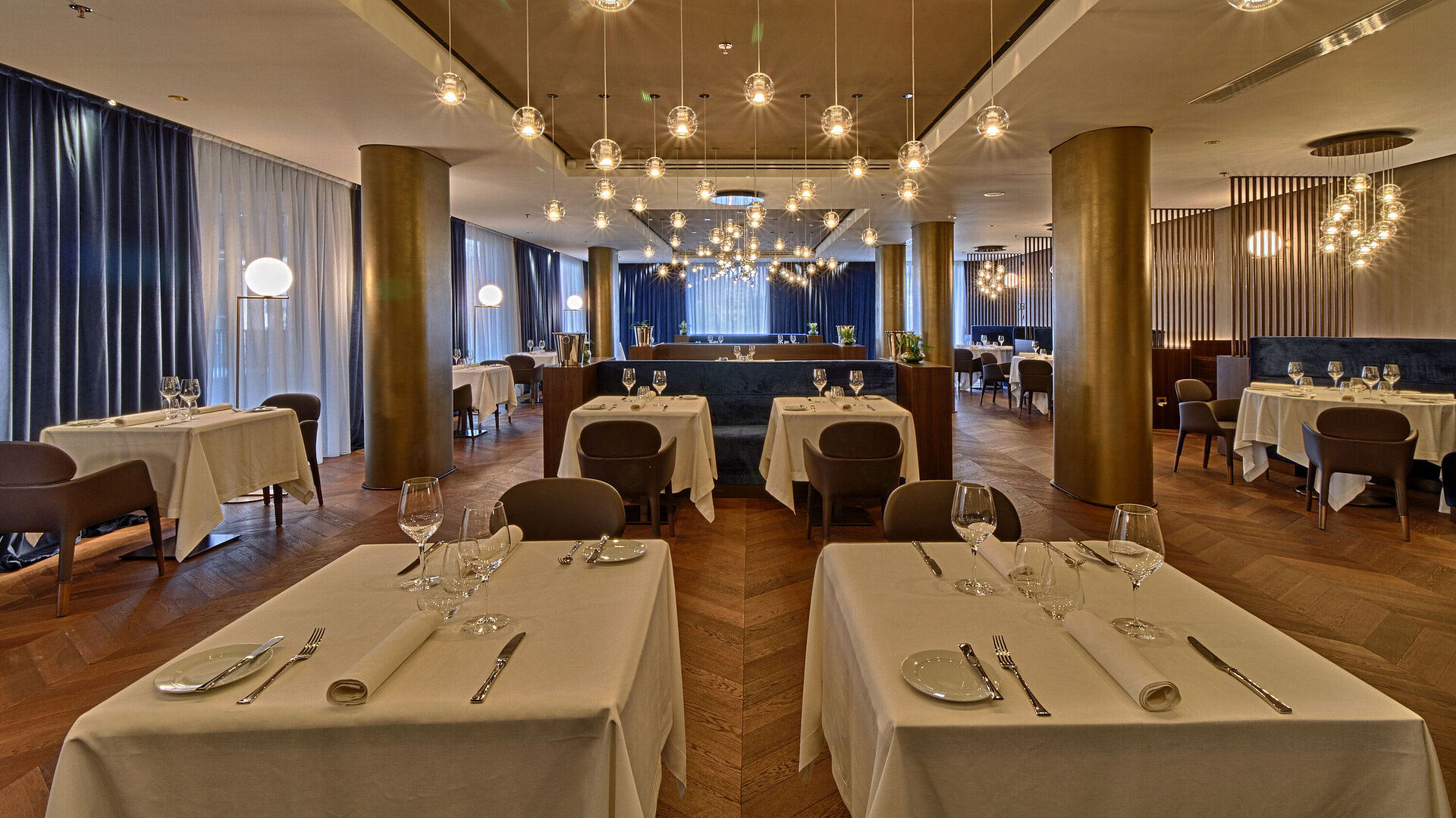 Spacious restaurant with elegant lighting, wooden floor and set tables at Maritim Hotel Plaza Tirana