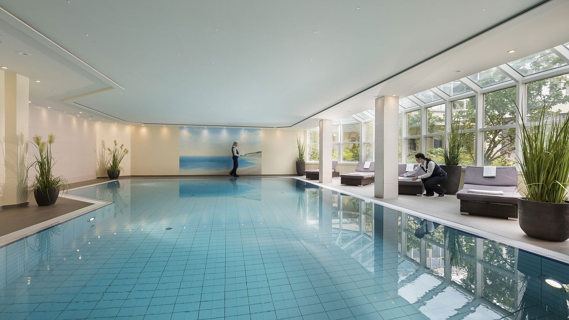 Large indoor pool at Maritim Hotel Würzburg with glass front, loungers and attentive service.
