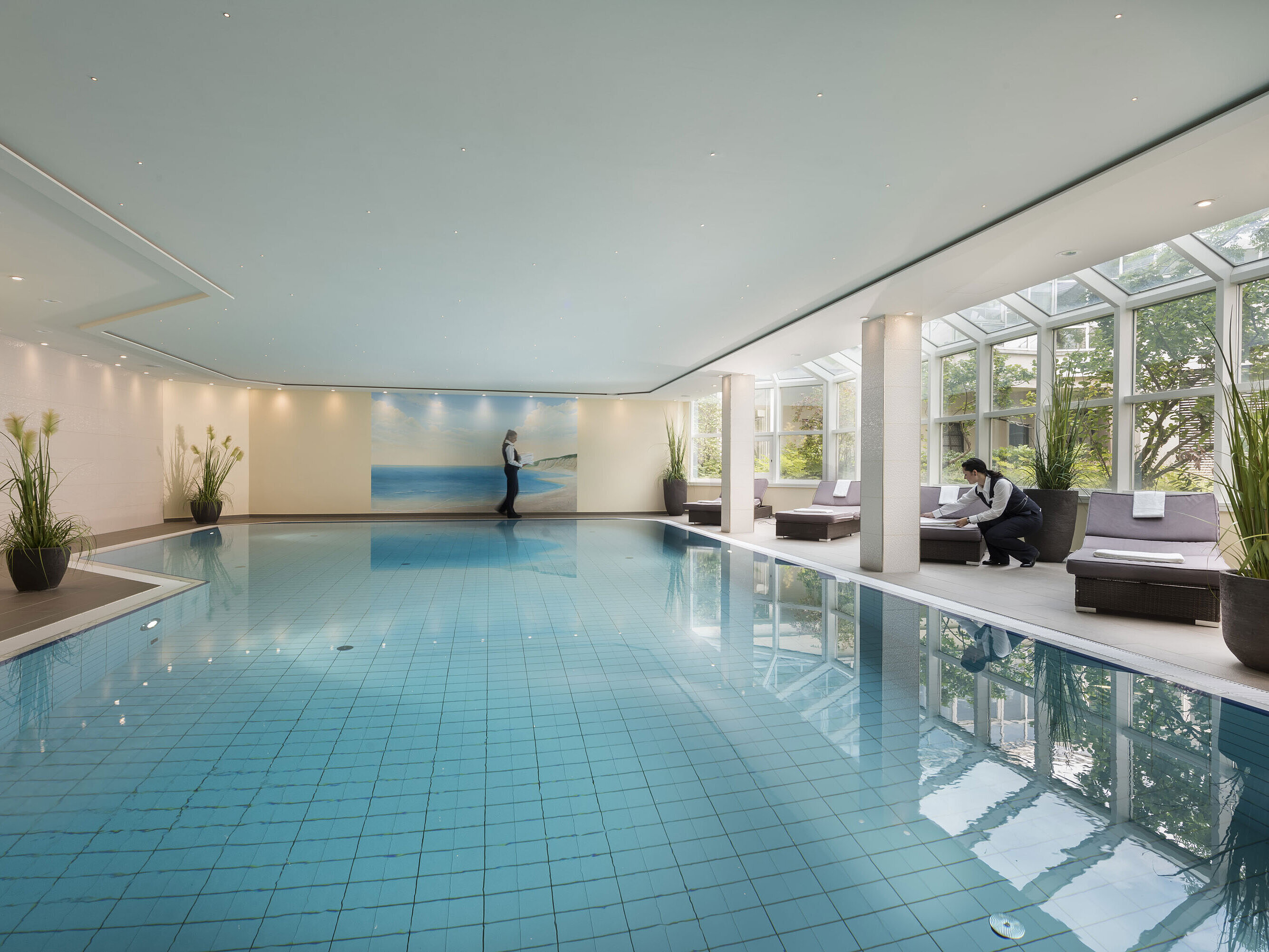 Large indoor pool at Maritim Hotel Würzburg with glass front, loungers and attentive service.