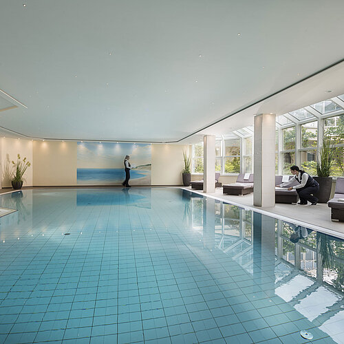 Large indoor pool at Maritim Hotel Würzburg with glass front, loungers and attentive service.