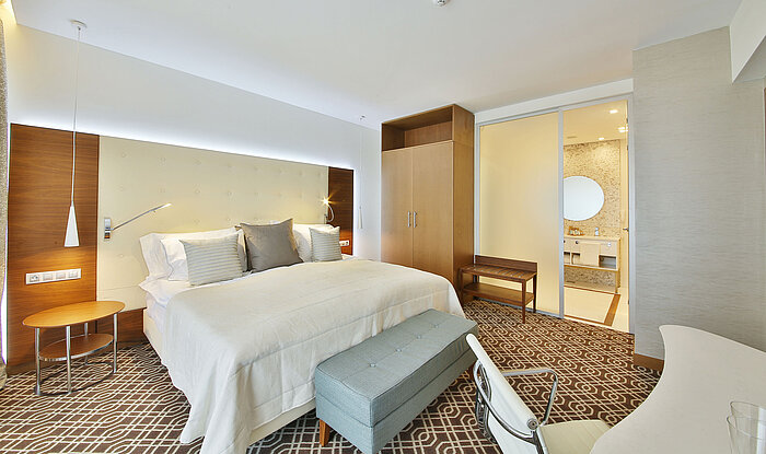 Elegant hotel room with large bed, warm wooden elements and view into the modern bathroom