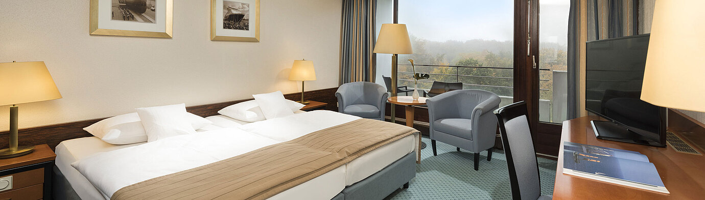 Classic room at the Maritim Hotel Kiel with large double bed, seating area, desk and balcony with a view of the countryside.