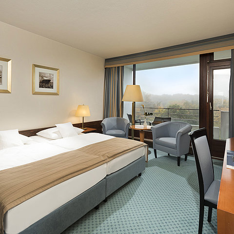 Classic room at the Maritim Hotel Kiel with large double bed, seating area, desk and balcony with a view of the countryside.