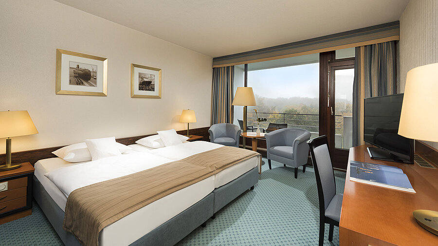 Classic room at the Maritim Hotel Kiel with large double bed, seating area, desk and balcony with a view of the countryside.