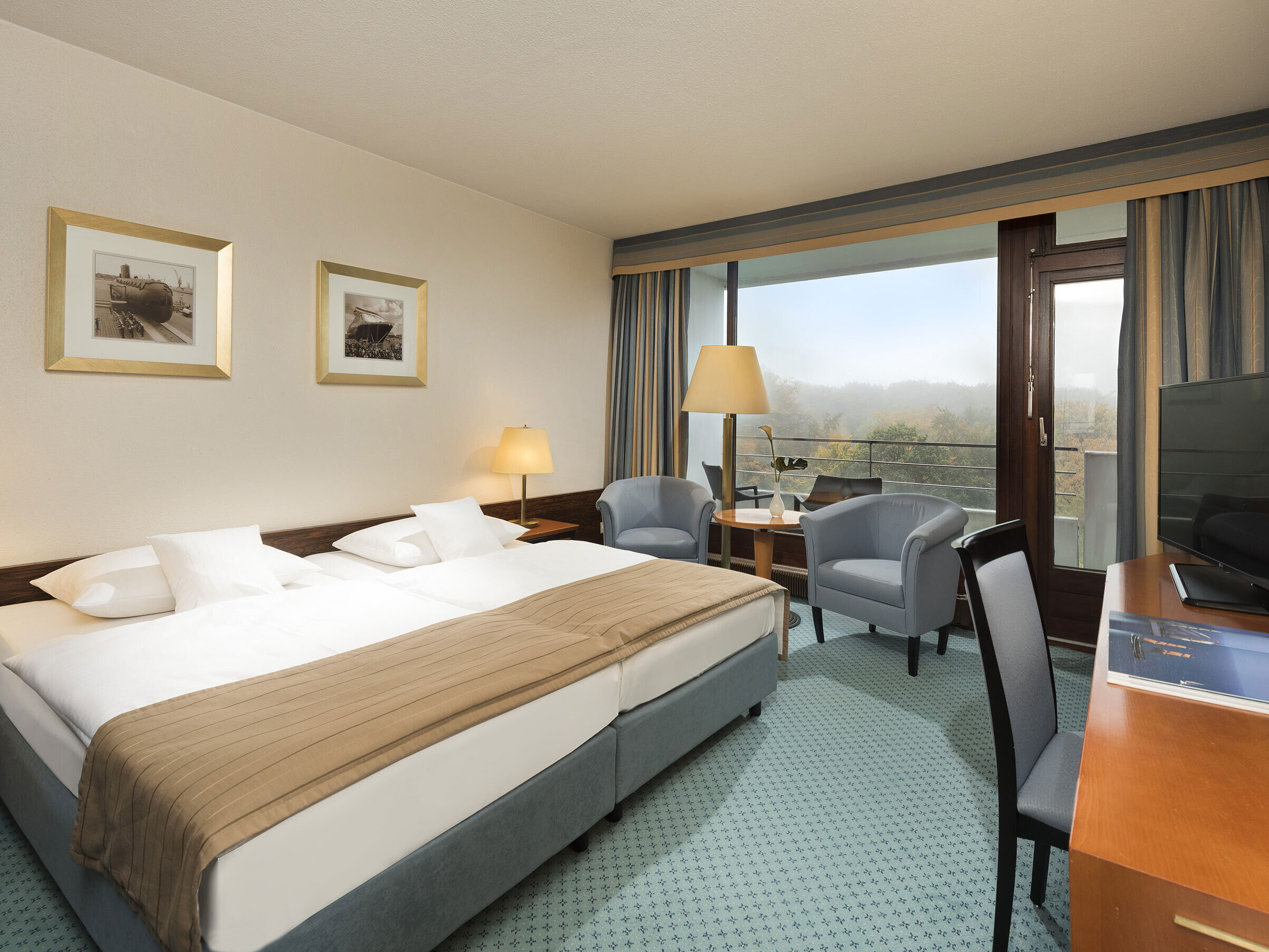 Classic room at the Maritim Hotel Kiel with large double bed, seating area, desk and balcony with a view of the countryside.