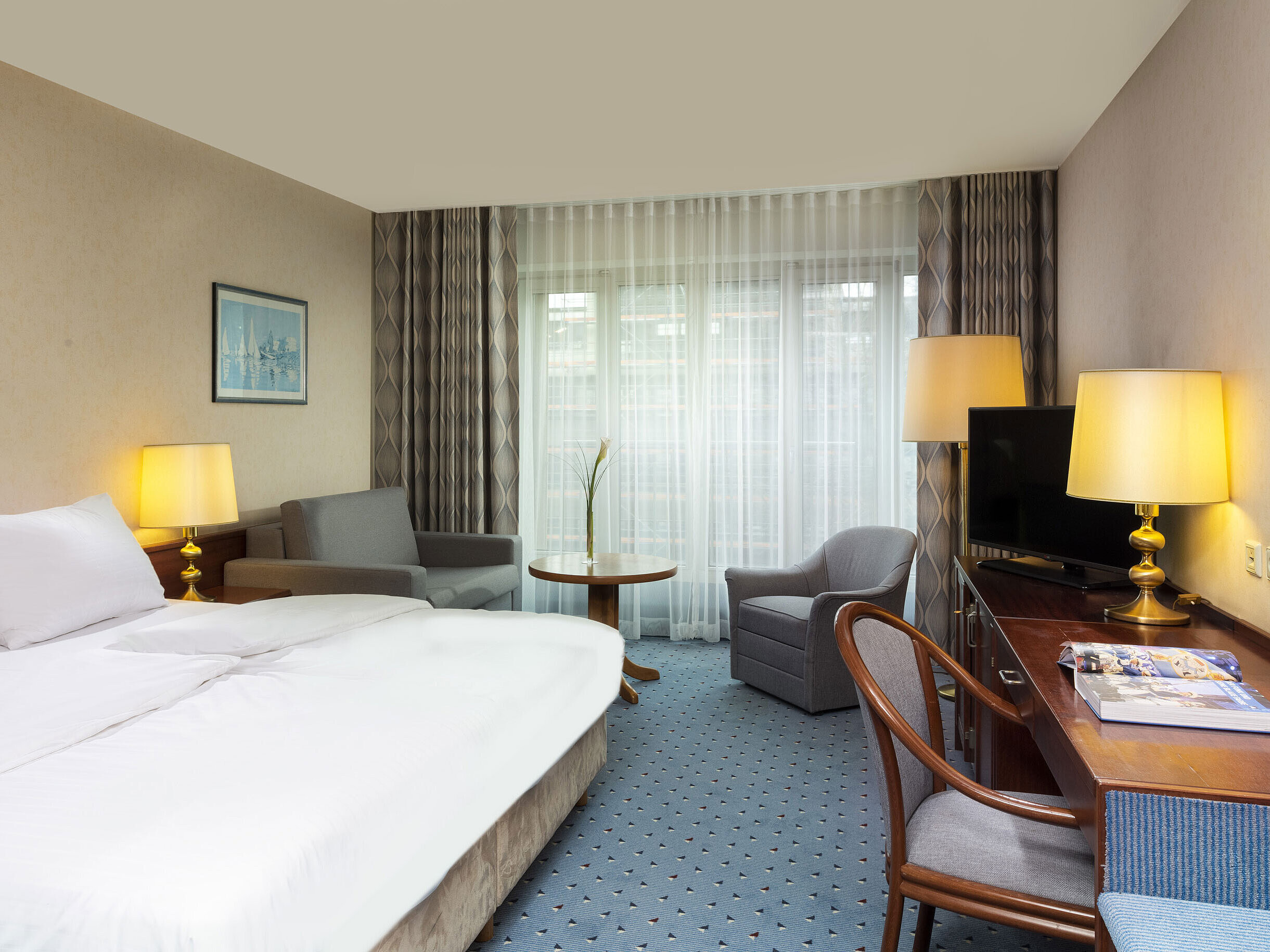 Comfort room at Maritim Hotel Cologne with a double bed, desk, sofa, and modern interior with large windows.