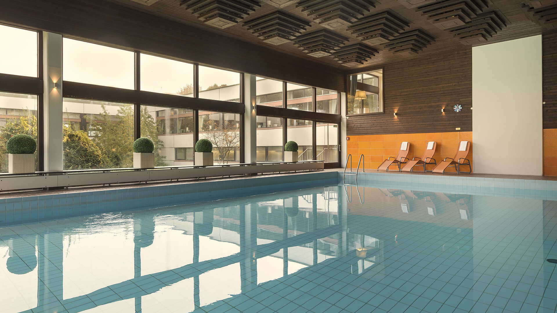 The picture shows the indoor pool of the Maritim Hotel Kiel, surrounded by large windows, with sun loungers for relaxation.