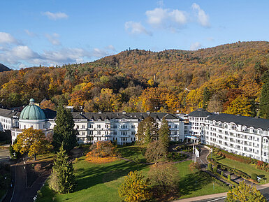 Exterior view of the Maritim Hotel Bad Wildungen surrounded by park, trees and an autumn forest panorama.