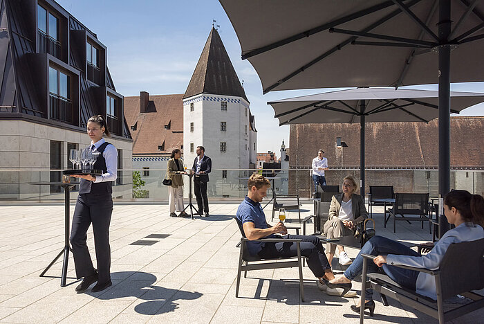 Guests enjoy drinks on the rooftop terrace of Maritim Hotel Ingolstadt with a view of the old town.
