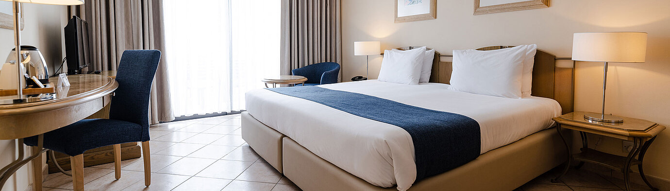 Bright double room with balcony, desk, seating area and floor-to-ceiling window