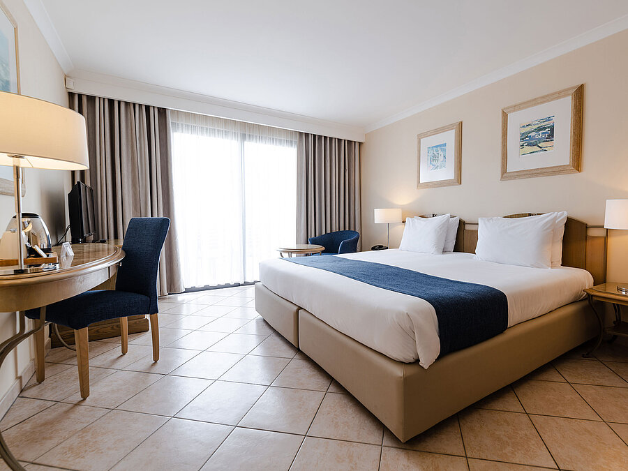 Bright double room with balcony, desk, seating area and floor-to-ceiling window