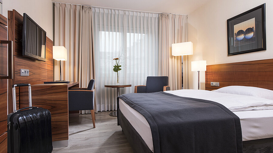 Cosy room with double bed, desk and suitcase at the Maritim Hotel Munich