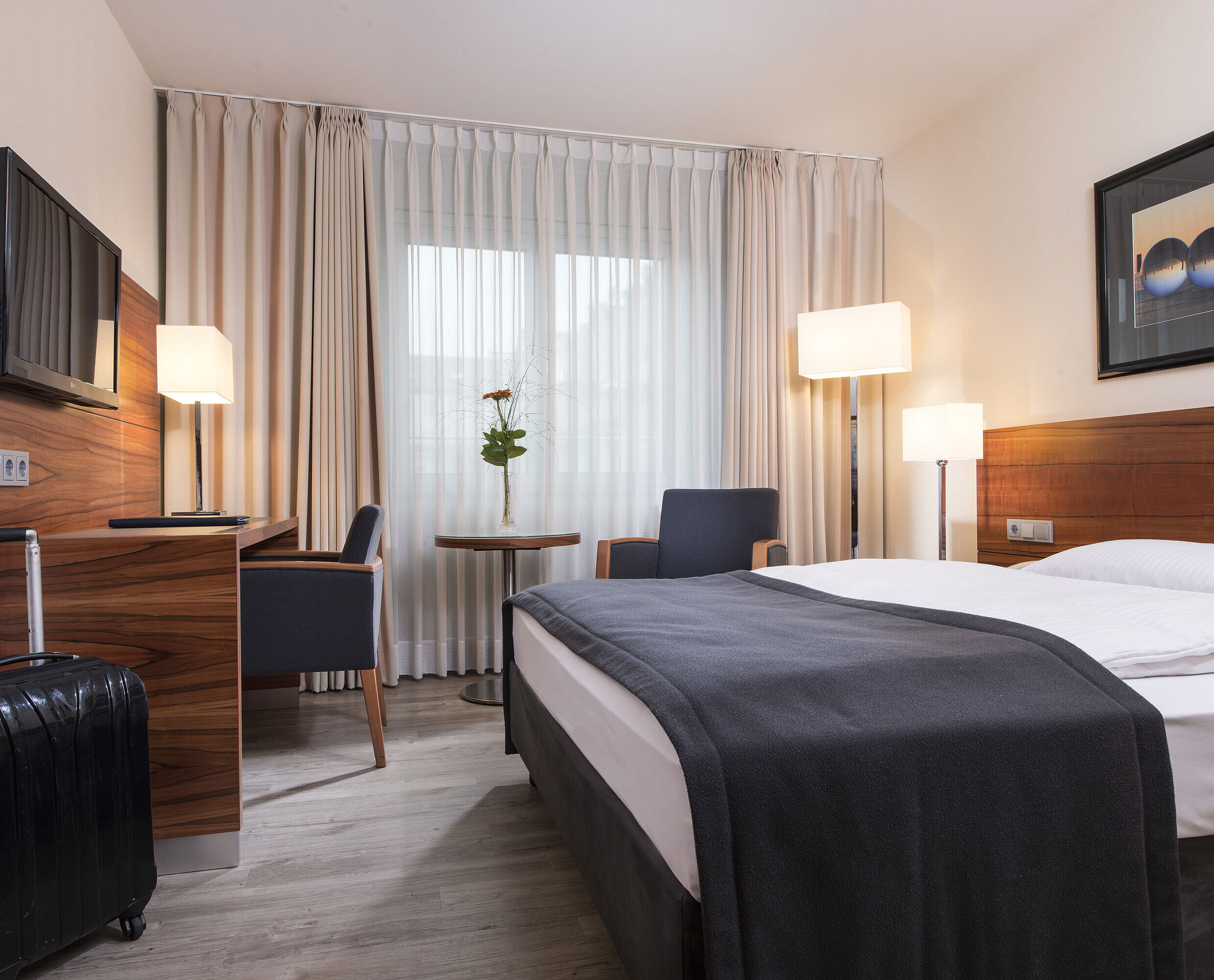 Cosy room with double bed, desk and suitcase at the Maritim Hotel Munich