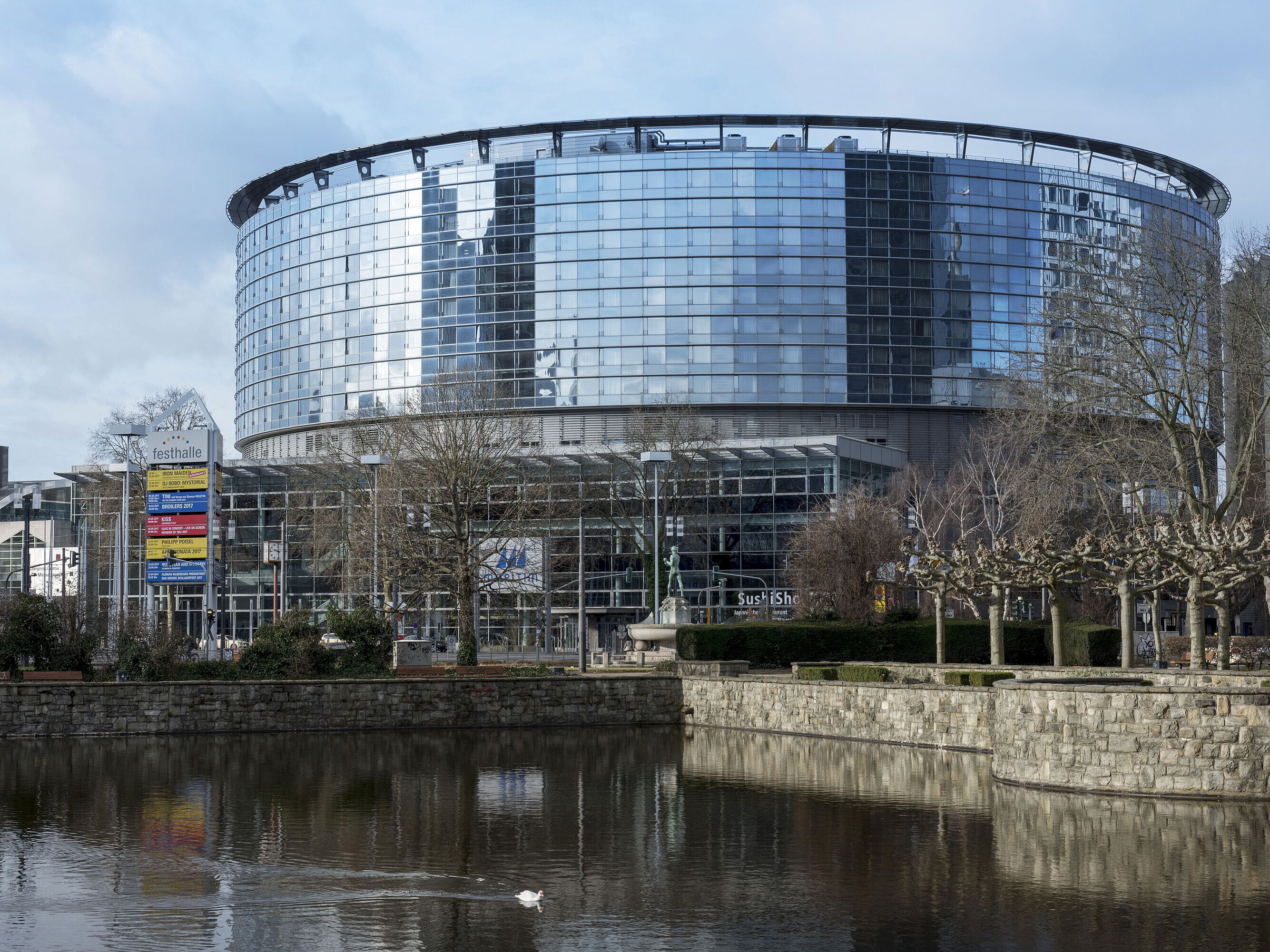 Exterior view of Maritim Hotel Frankfurt with modern glass facade and adjacent pond in daylight.
