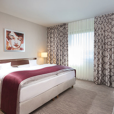 Spacious suite at Maritim Hotel Bonn with a cozy double bed, modern decor, and a wine-red bed runner.