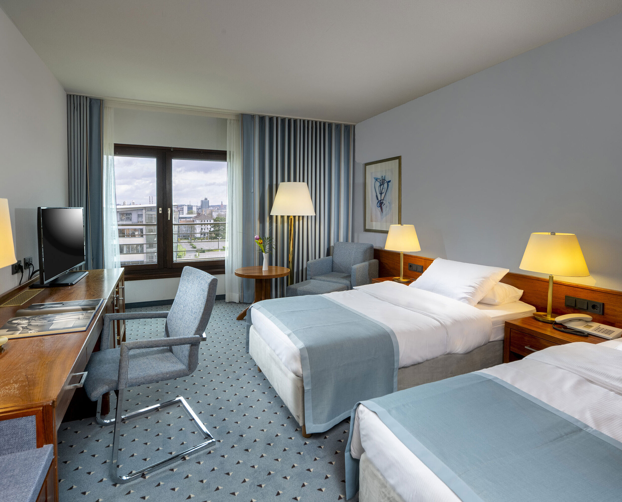Comfort twin room at Maritim Hotel Darmstadt with desk, two single beds, and panoramic window with city view.