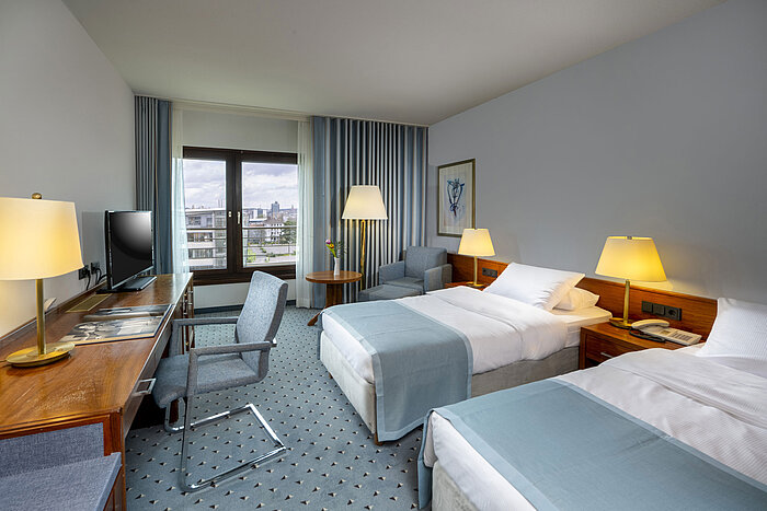 Comfort twin room at Maritim Hotel Darmstadt with desk, two single beds, and panoramic window with city view.