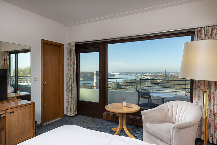 Bright hotel room with balcony, desk and view of the Trave River and Lübeck Bay  FR: